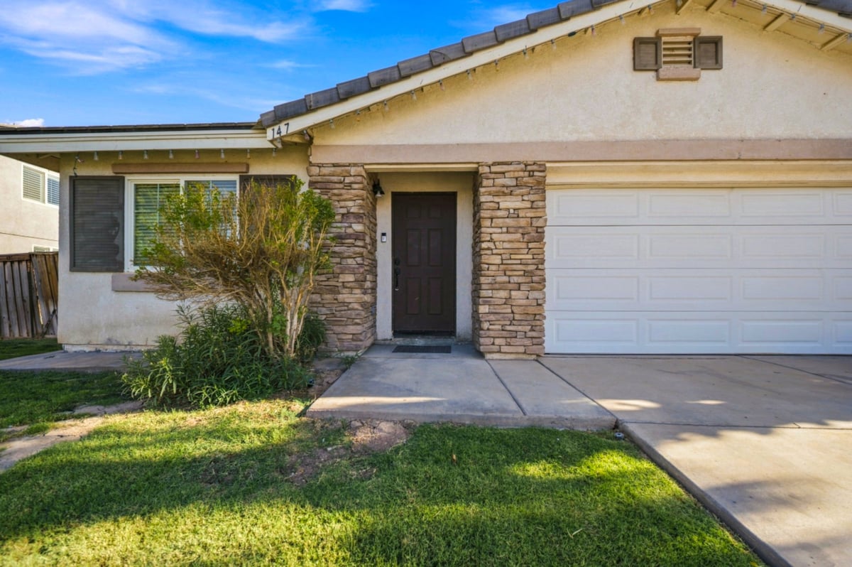 Single-story house with white stucco and brick facade, white garage door, black front door, manicured lawn, and clear blue sky