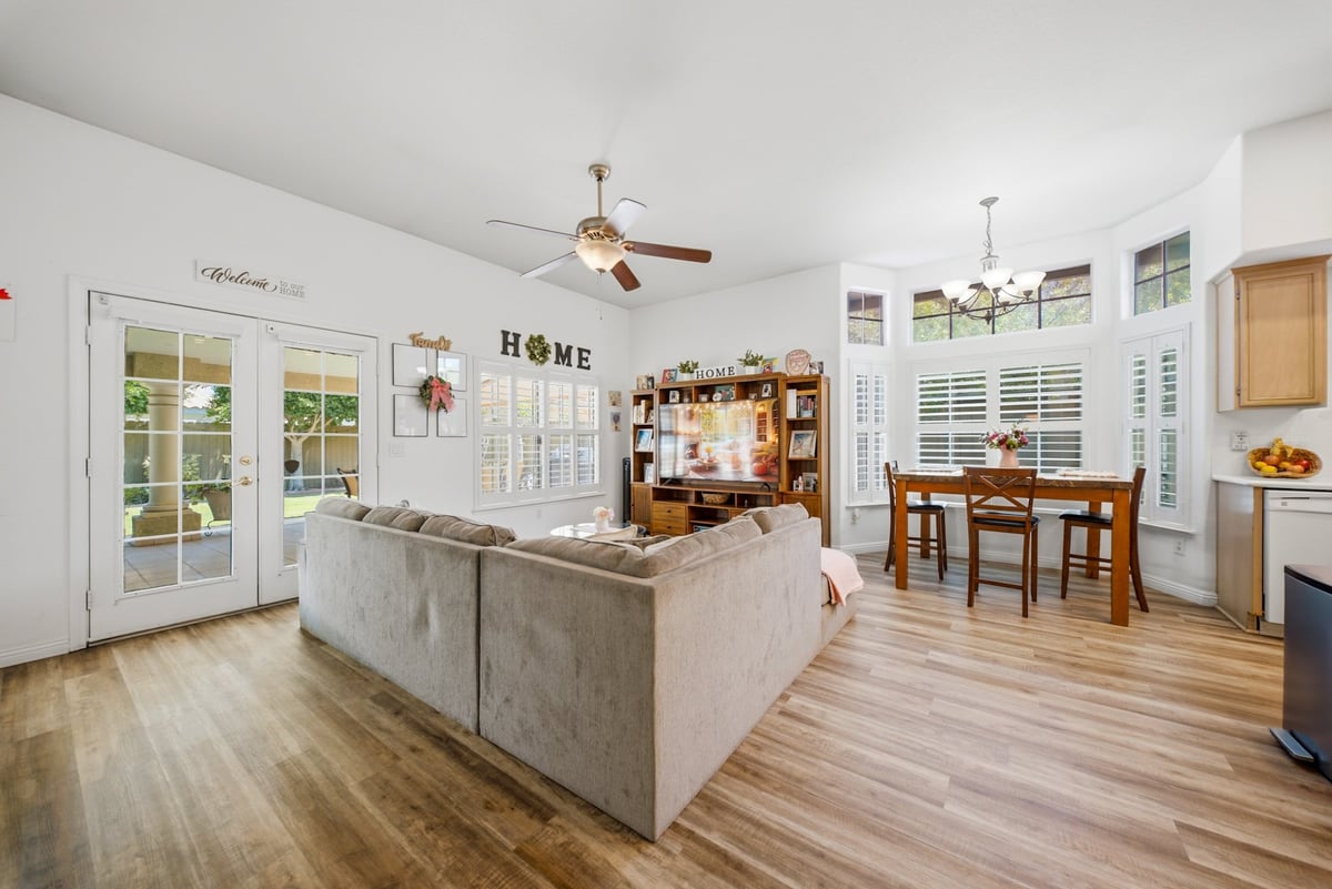 Bright open-concept living room and kitchen with gray island, wood flooring, ceiling fans, french doors, and dining area