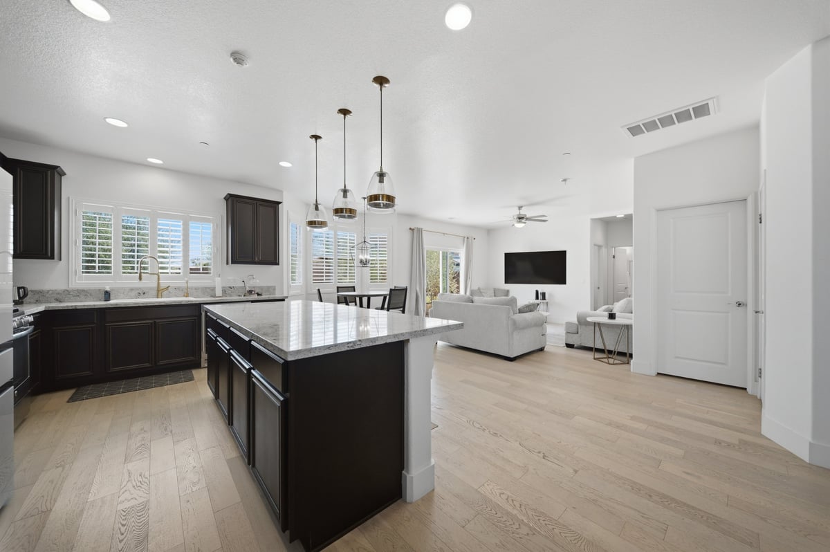 Modern open-concept kitchen and living room with black island, white cabinetry, hardwood floors, and pendant lighting