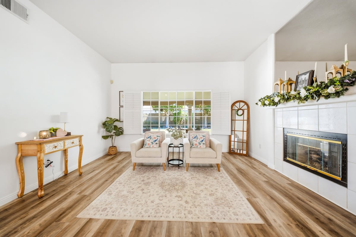 Bright, modern living room with beige armchairs, fireplace, hardwood floors, and large windows overlooking a garden