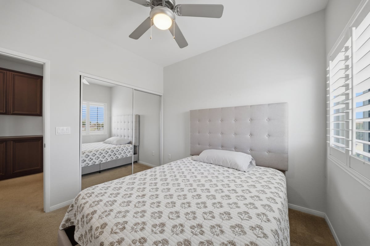 Modern bedroom with queen bed, mirrored closet doors, ceiling fan, and shuttered windows