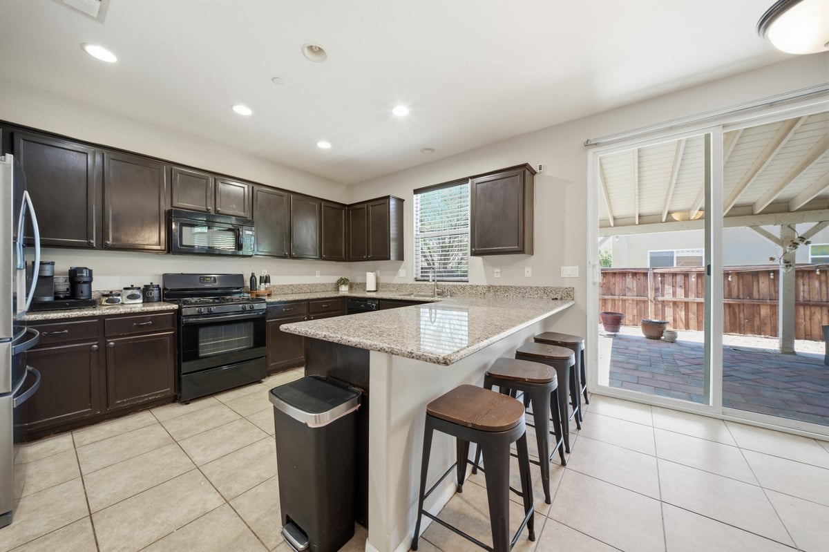 Modern kitchen with dark wood cabinets, granite countertops, island with bar seating, and glass doors leading to outdoor patio