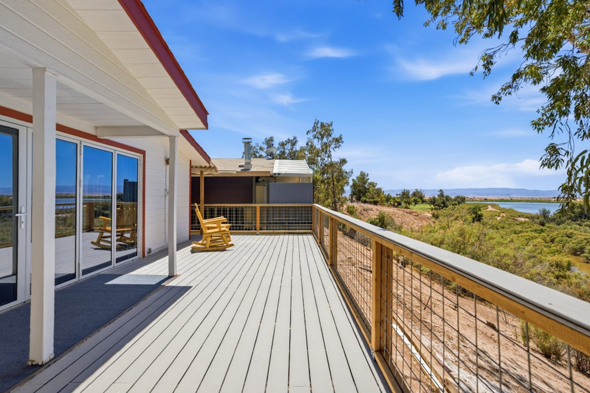 Modern deck with white railings overlooking scenic waterfront view with yellow Adirondack chair and green landscaping