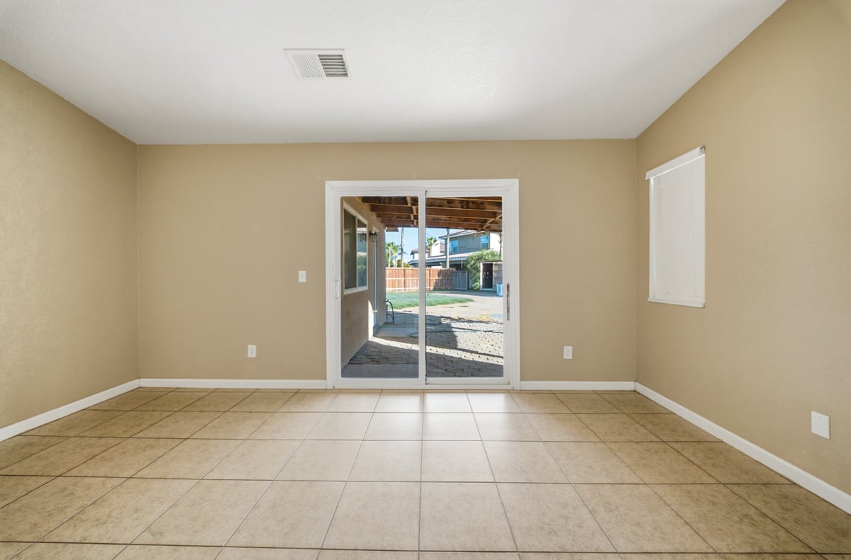 Empty room with beige walls, tile flooring, and glass doors leading to patio outside