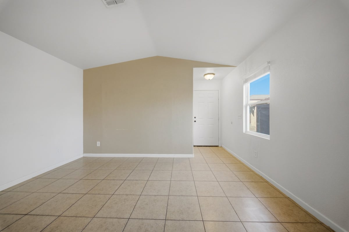 Empty room with beige walls, tile and wood flooring, white refrigerator, and window with blue sky view
