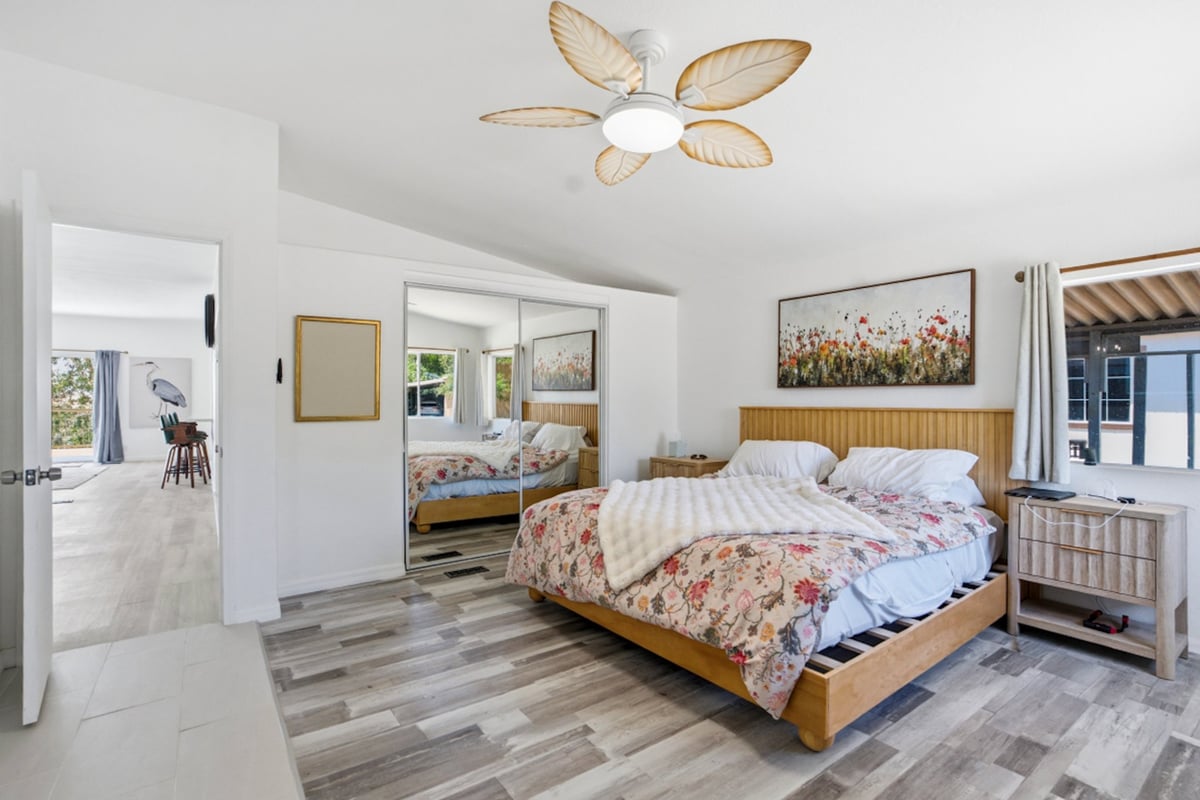 Modern master bedroom with wooden bed, floral bedding, decorative ceiling fixture, mirrored closet doors, and hardwood flooring