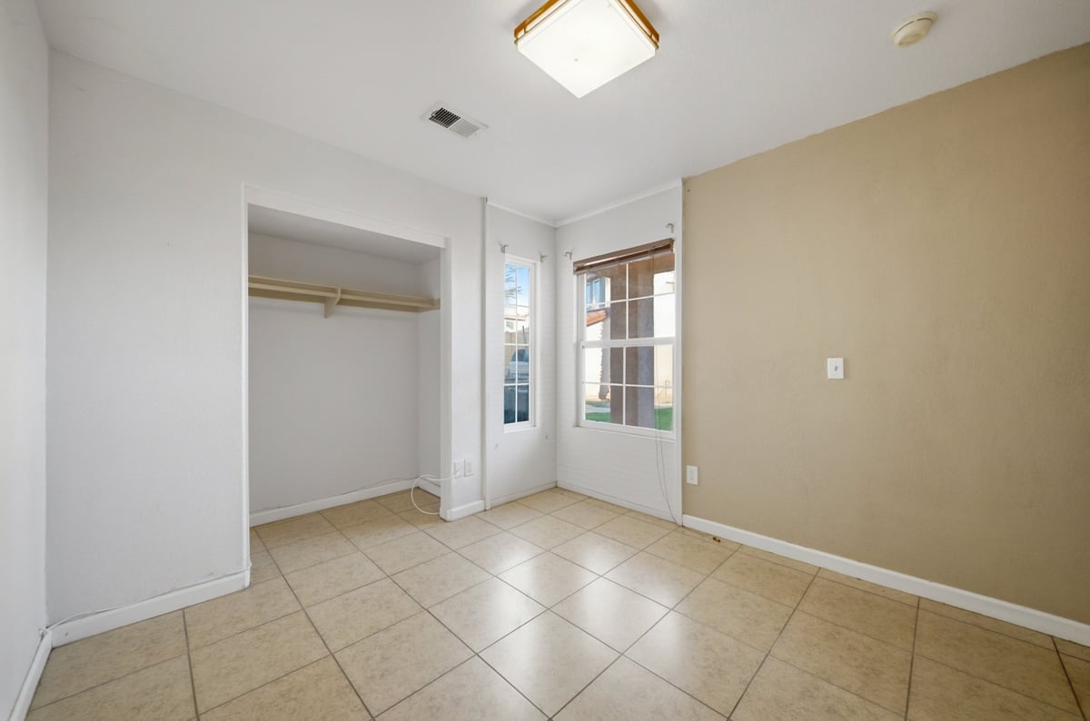 Empty bedroom with tile flooring, open closet, and French doors leading to a sunlit patio