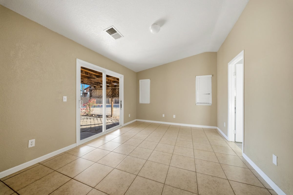 Empty beige room with tile flooring, glass doors leading to patio, and white trim