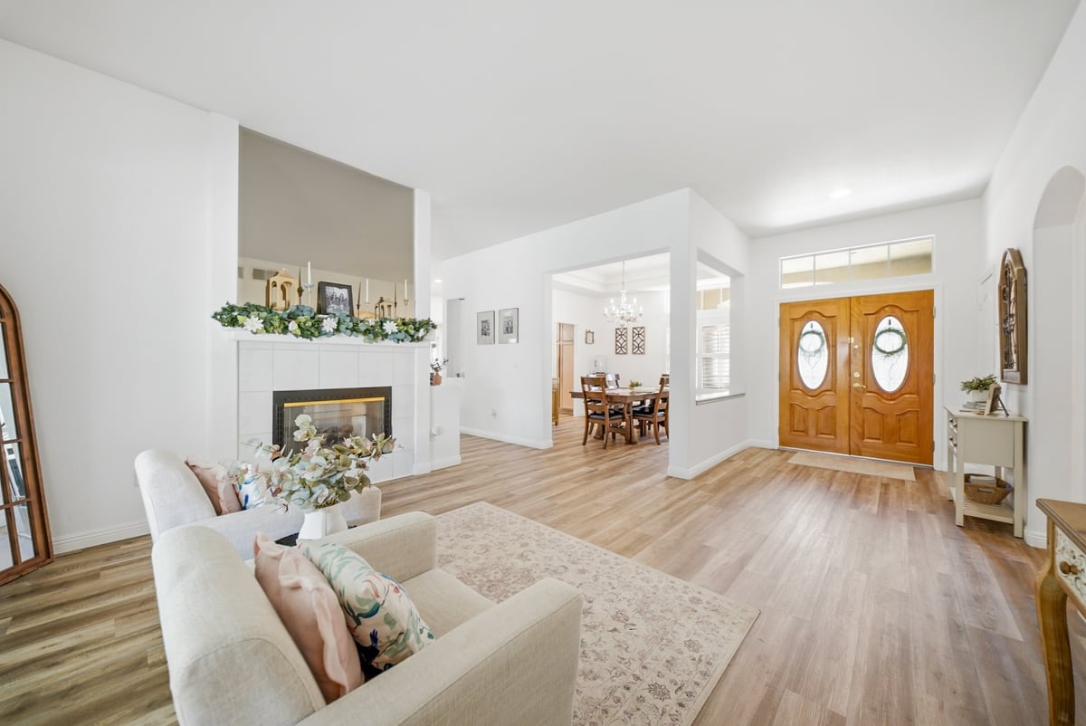 Bright open-concept living room with white furniture, hardwood floors, fireplace, and large double doors leading to dining area