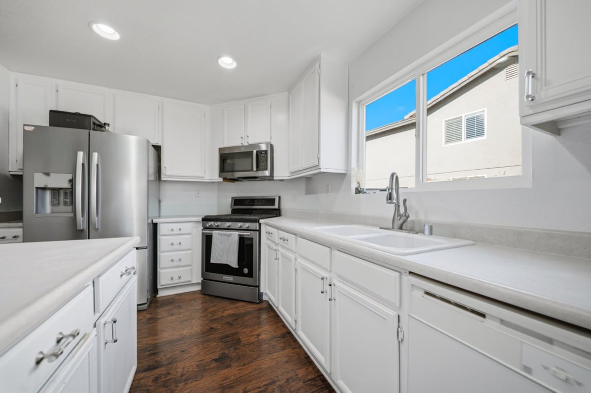 Modern white kitchen with stainless steel appliances, white cabinets, and wood flooring