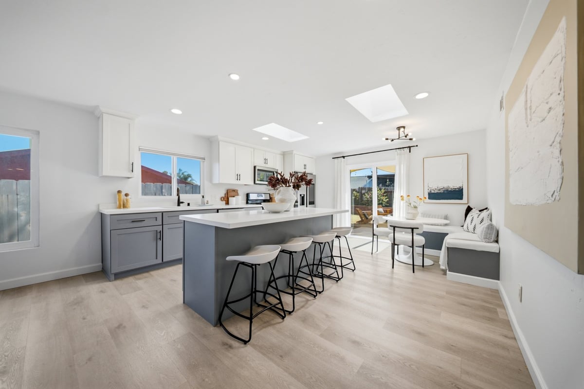 Modern kitchen and dining area with island seating, light wood flooring, white cabinetry, and sliding glass doors leading to patio