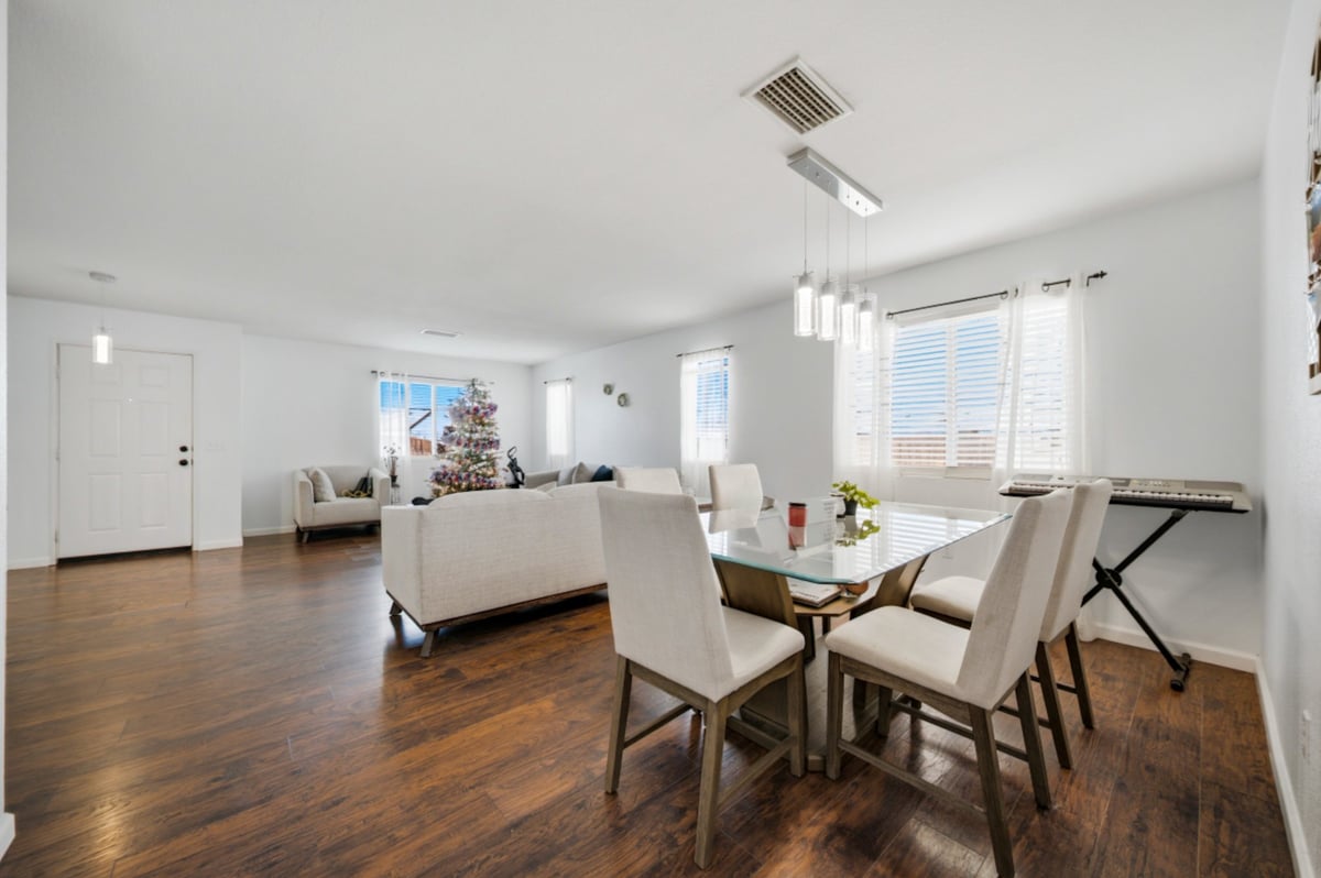 Modern open-concept apartment interior with dining table, cream sofa, hardwood floors, and large windows providing natural light