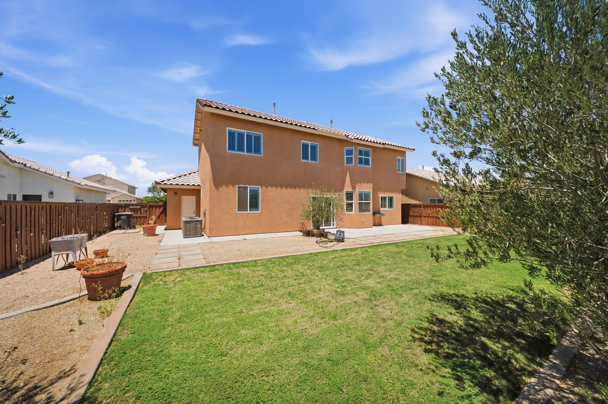 Orange terracotta house with blue shutters, patio area, and green lawn under clear blue sky