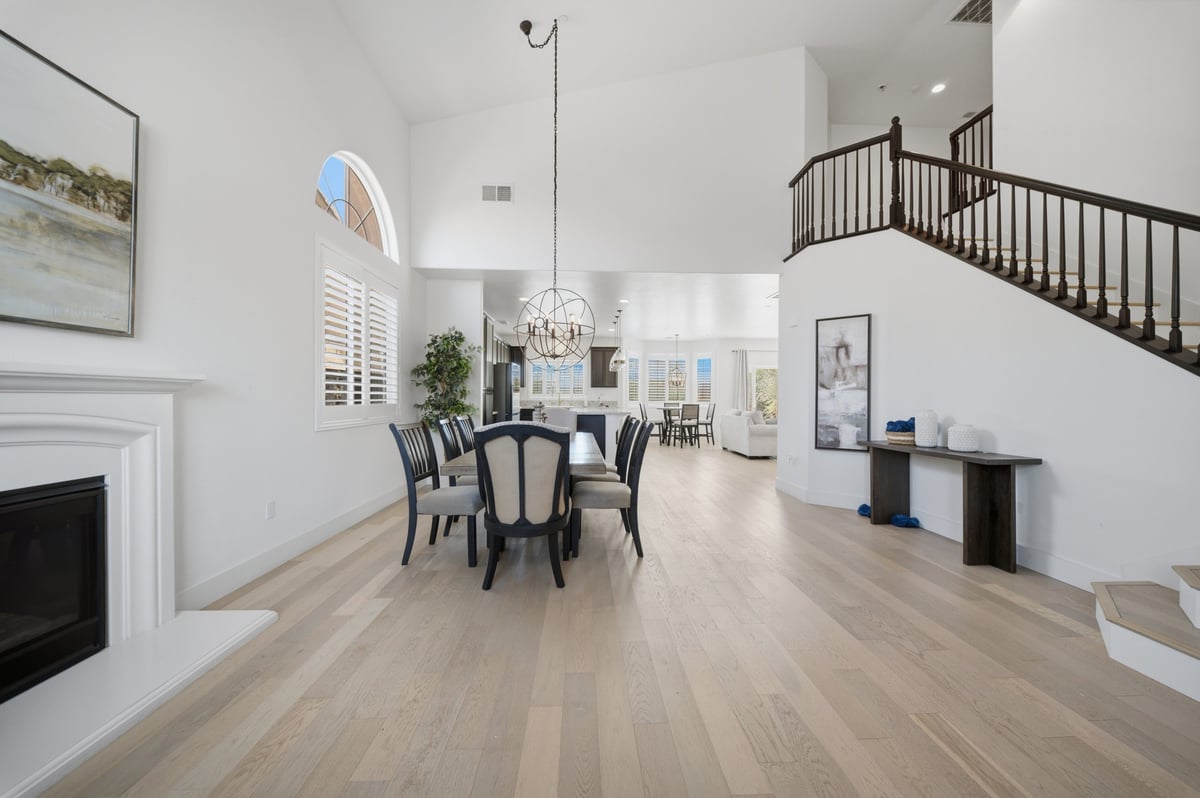 Spacious modern dining area with black chairs around round table, light wood flooring, white walls, fireplace, and spiral staircase in bright home interior