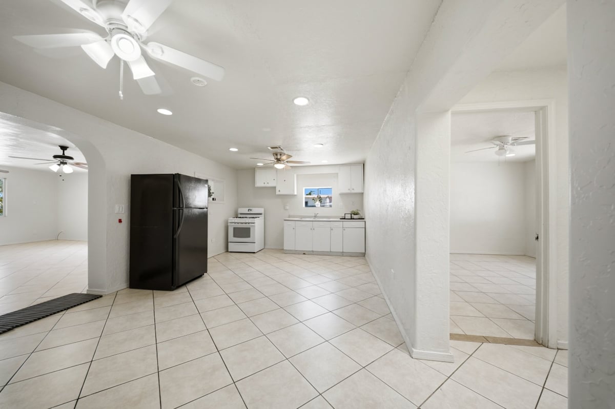 Spacious white kitchen with beige tile flooring, black refrigerator, white cabinets, and ceiling fans