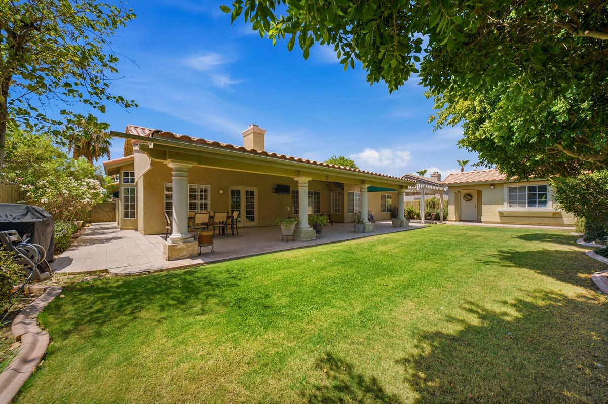 Beige single-story house with covered porch overlooking a spacious manicured lawn under blue sky