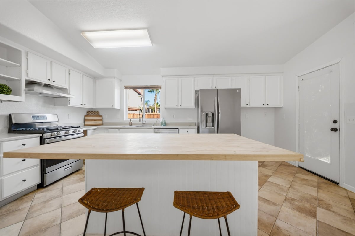 Modern white kitchen with wood countertop island, stainless steel appliances, and two wooden bar stools