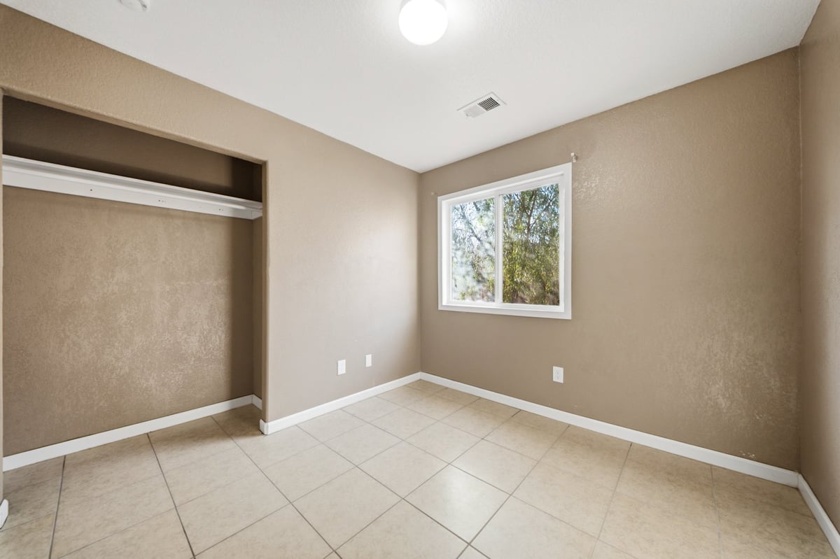 Empty bedroom with beige walls, tile flooring, closet, window with natural light, and recessed ceiling light