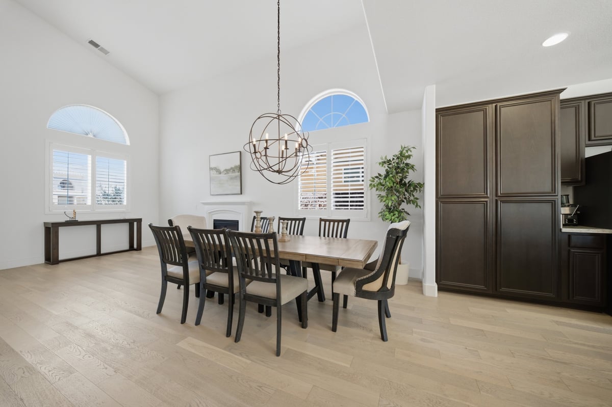 Modern dining room with dark wood table, black chairs, pendant light, arched windows, and open kitchen area with white walls and light hardwood flooring