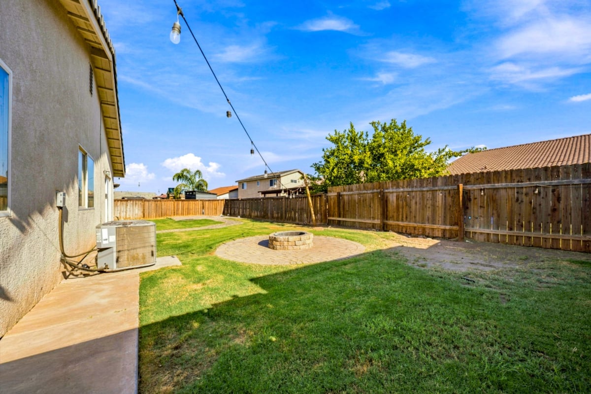Spacious backyard with green grass, wooden fences, patio area, and clear blue sky
