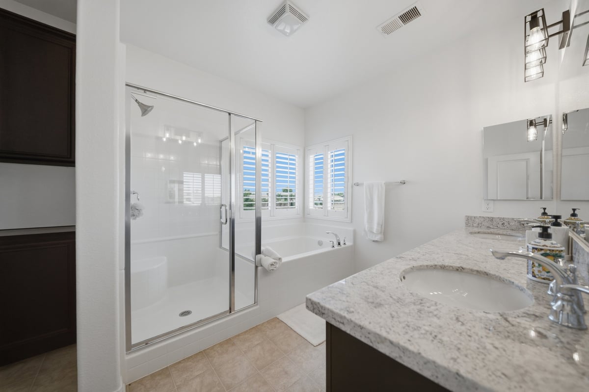 Modern bathroom with marble countertop, glass shower enclosure, double vanity sink, and shuttered window