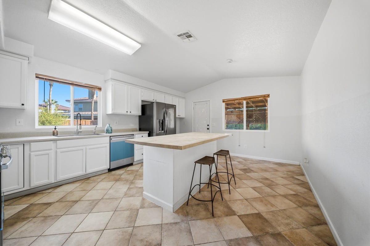 Bright modern kitchen with white cabinets, island, stainless steel appliances, and tile flooring with windows