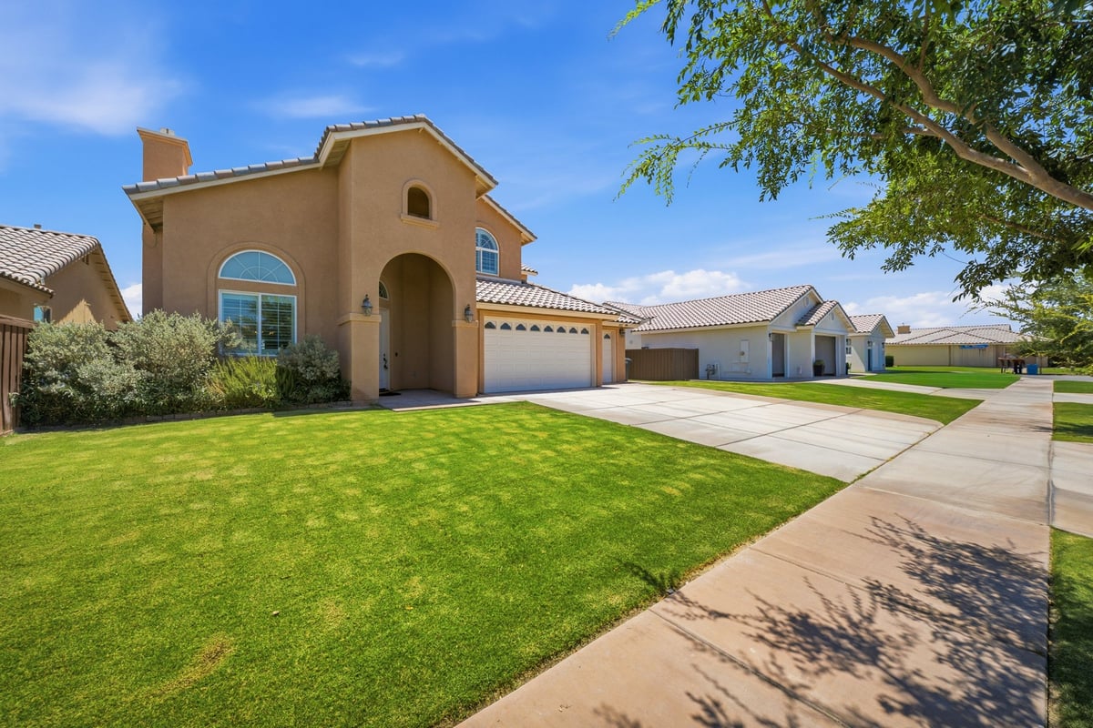 Spacious two-story tan stucco home with arched entryway, manicured lawn, and circular driveway on sunny day