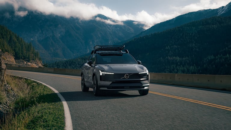 Modern Volvo SUV driving on mountain road with scenic peaks and forested valleys in background