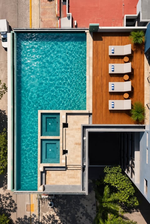 Aerial view of modern residential building with turquoise swimming pool, wooden deck with lounge chairs, and contemporary architecture