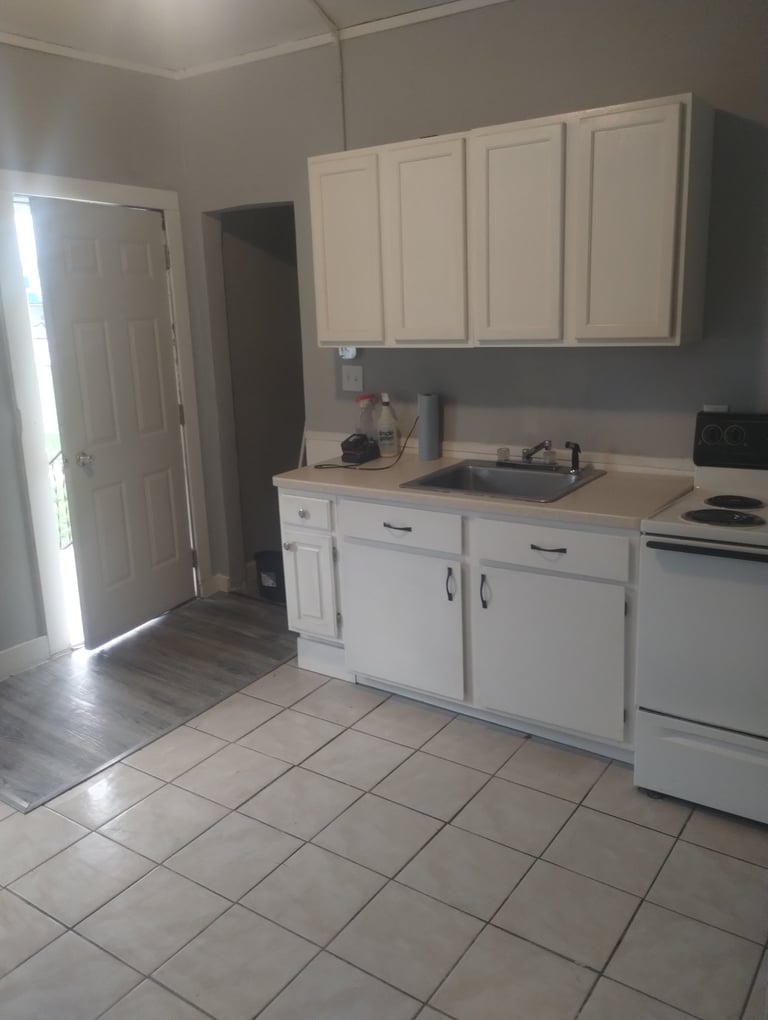 White kitchen with beige countertops, tile flooring, cabinet storage, and white appliances including stove and sink