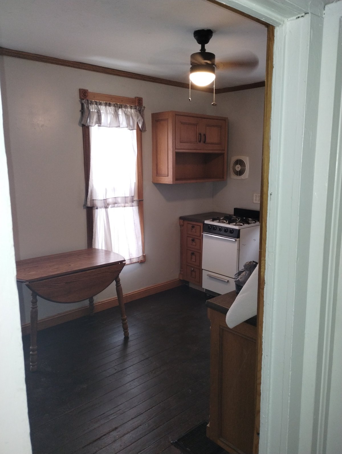 Small kitchen interior with dark wood flooring, drop-down table, vintage stove, and window with curtains