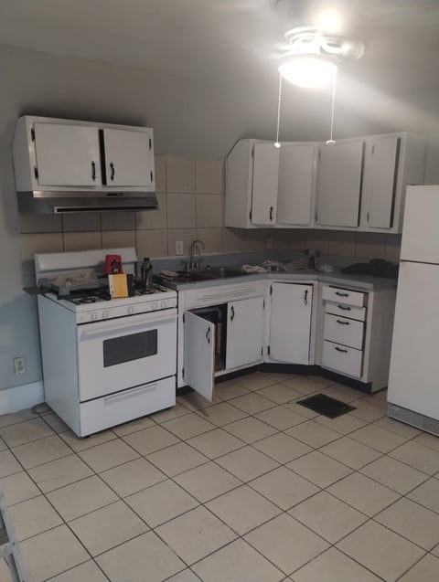 Small kitchen with white cabinets, stove, and appliances on beige tile flooring with overhead lighting