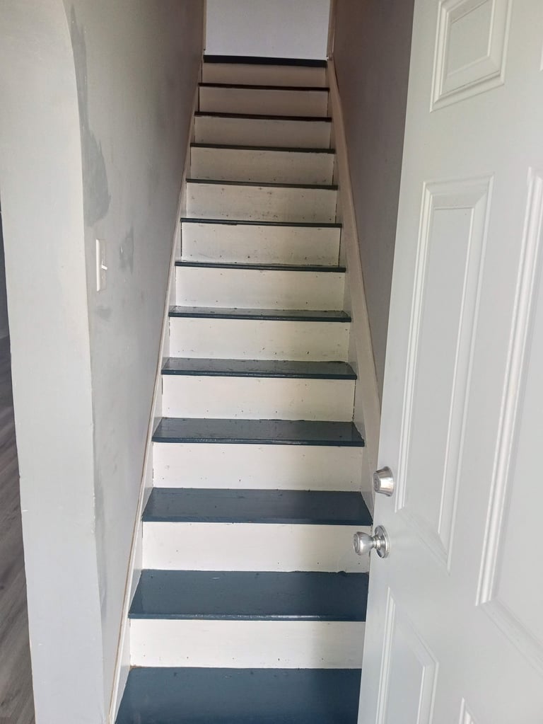 Interior staircase with alternating light wood and dark metal treads, white walls, and two white doors visible along the sides