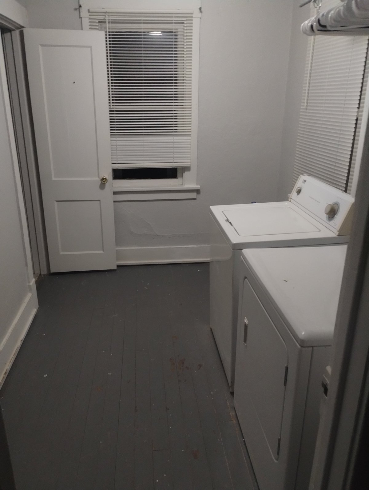 Small laundry room with white washer and dryer, window with blinds, and dark floor