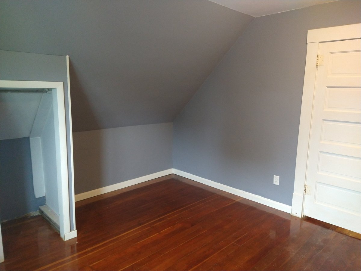 Empty upstairs bedroom with sloped ceiling, hardwood floors, white trim, and pale blue walls with two doors