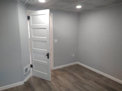 Empty room with white five-panel door, gray walls, wood laminate flooring, and recessed ceiling lights