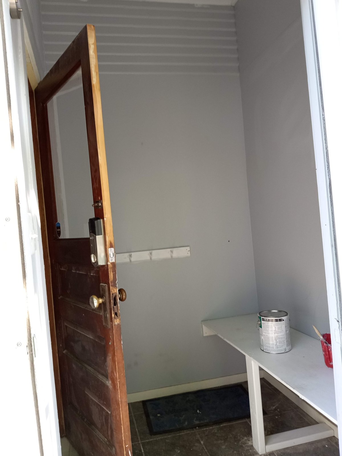Interior of small room with open dark wooden door, white walls, bench, and paint can on shelf