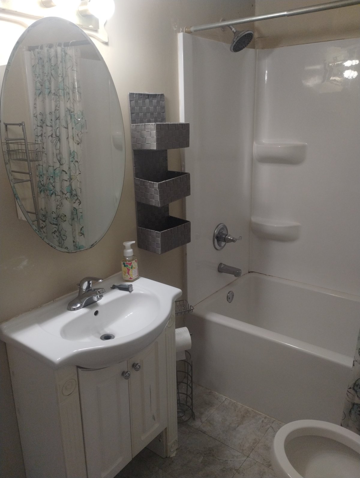 Modern bathroom with white pedestal sink, round mirror, glass shower enclosure, and black wall-mounted shelving