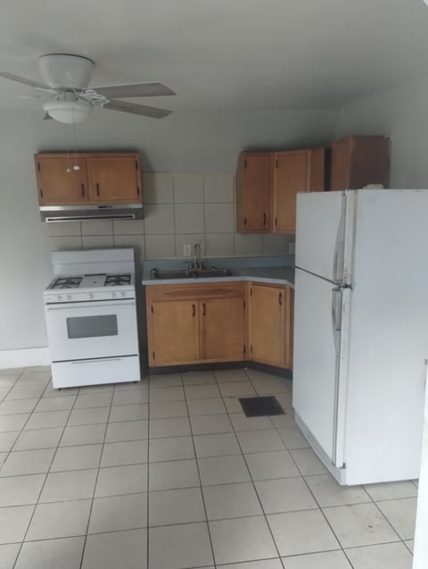 Small apartment kitchen with white stove, refrigerator, wooden cabinets, and ceiling fan