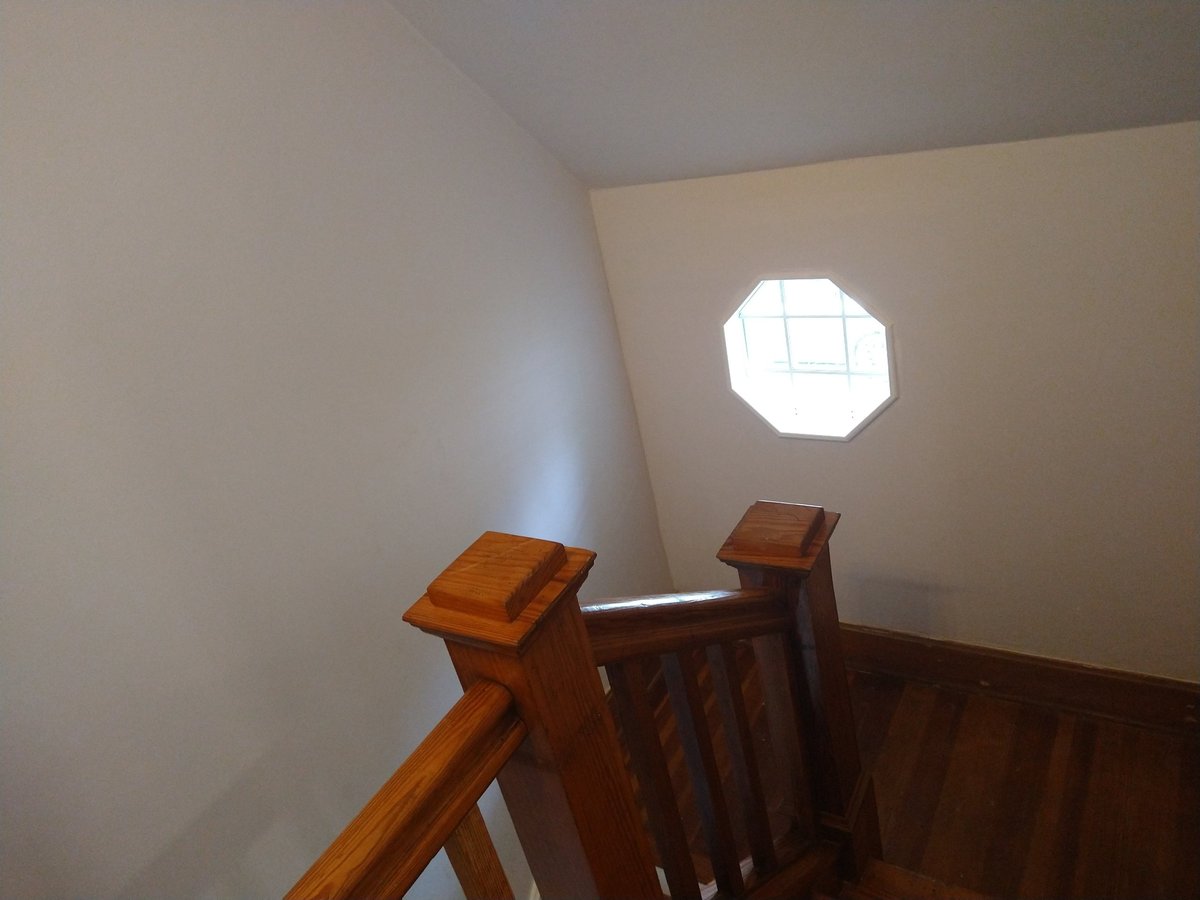 Interior view of wooden staircase with a glowing white octagonal window on beige wall illuminating the stairwell