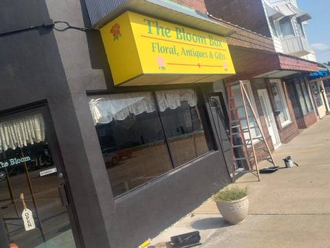 Yellow storefront sign for The Bloom Pad floral shop on a brick and concrete building with glass windows