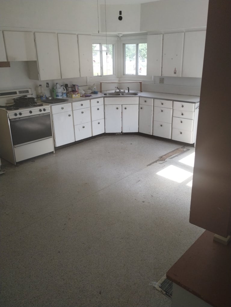 Empty kitchen with white cabinets, stainless steel appliances, and dual windows overlooking trees