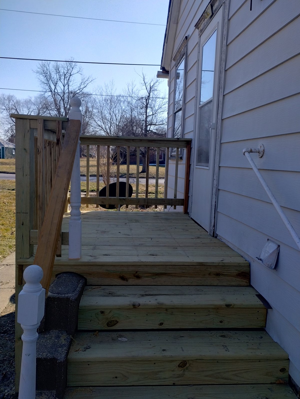 Wooden deck with steps and railing attached to a white mobile home, bare trees visible in background