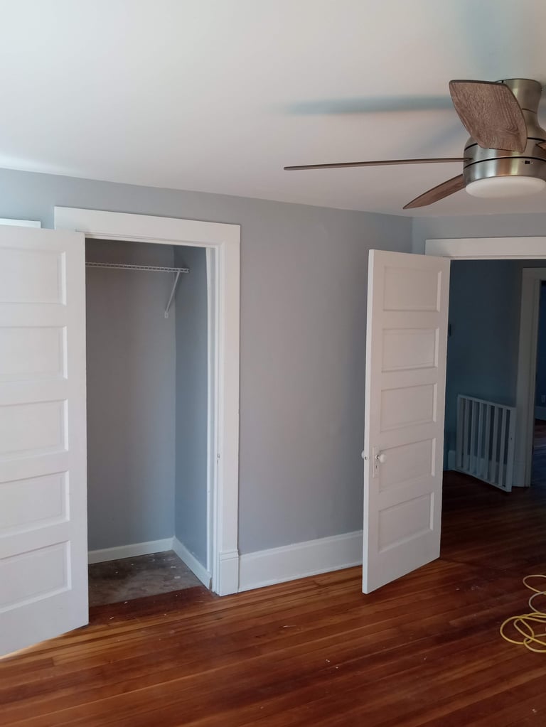 Empty bedroom with two open white closet doors, wood flooring, gray walls, and ceiling fan