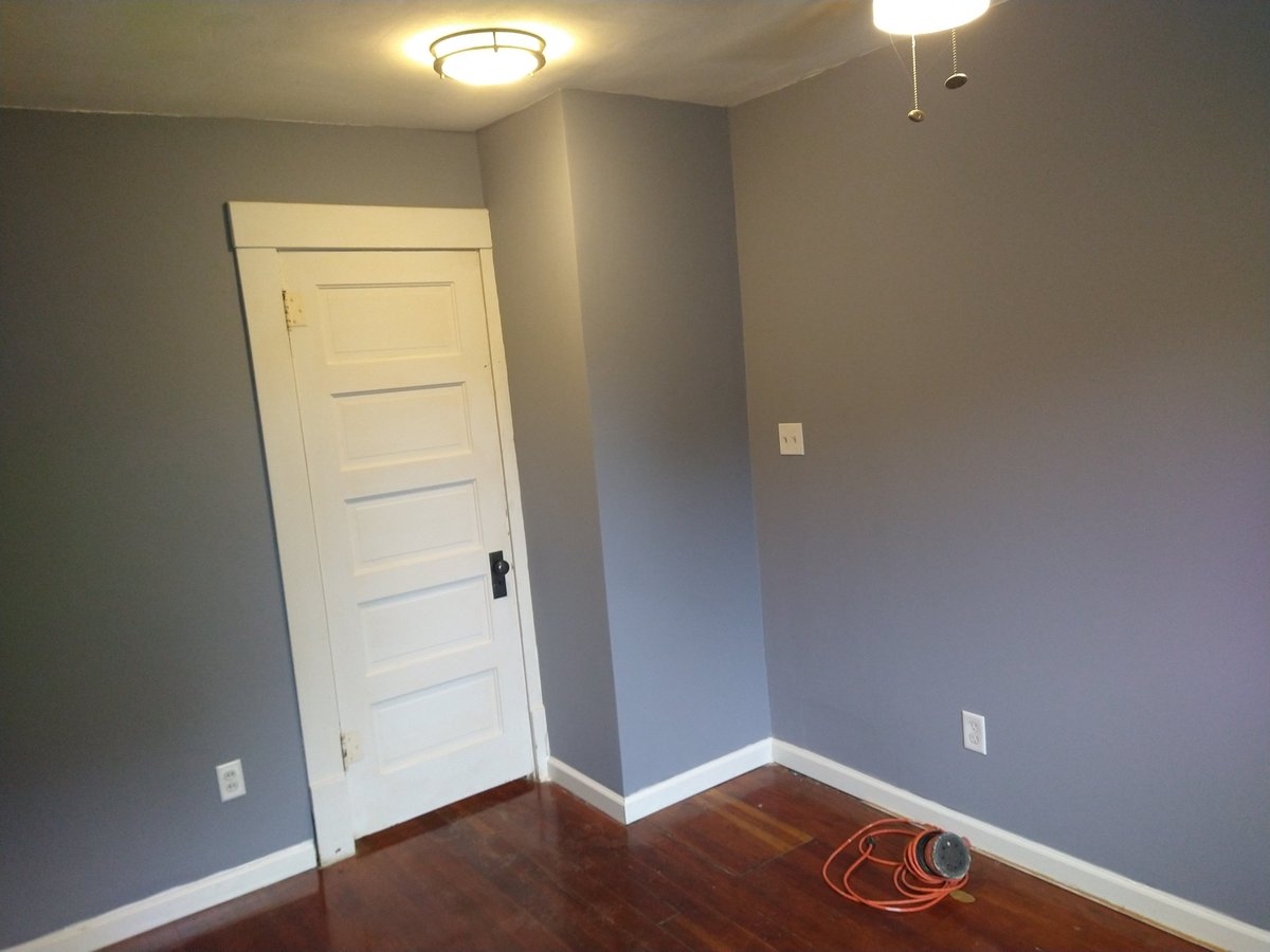 Empty bedroom with gray walls, white five-panel door, hardwood floor, and ceiling light fixtures
