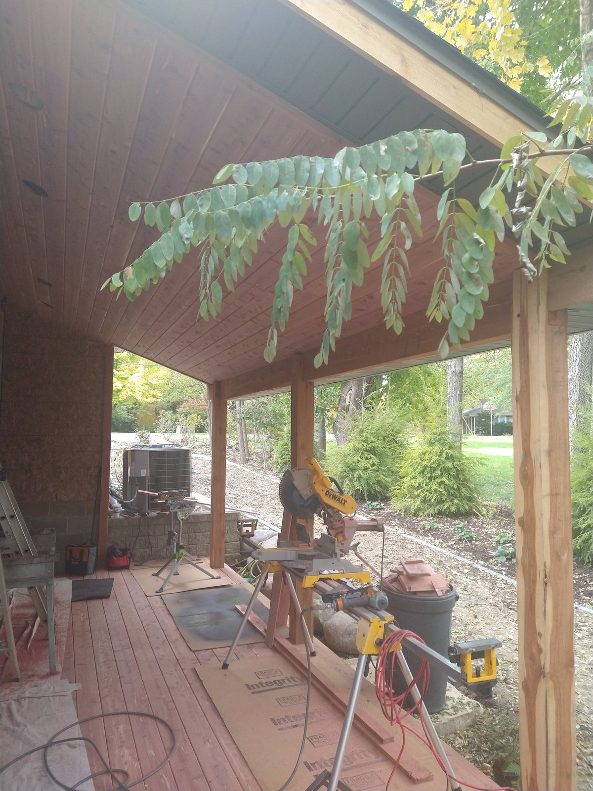 Covered porch under construction with hanging hops, woodworking tools scattered on the floor, and a DeWalt miter saw set up