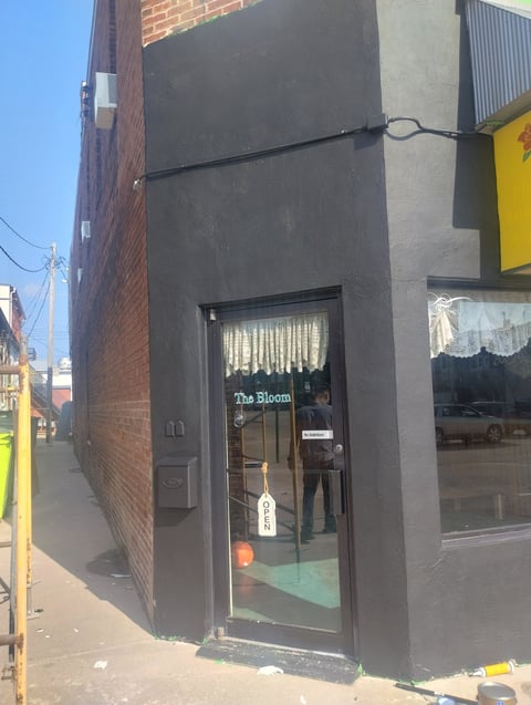 Narrow storefront with dark gray facade and black entrance door on a brick urban street corner