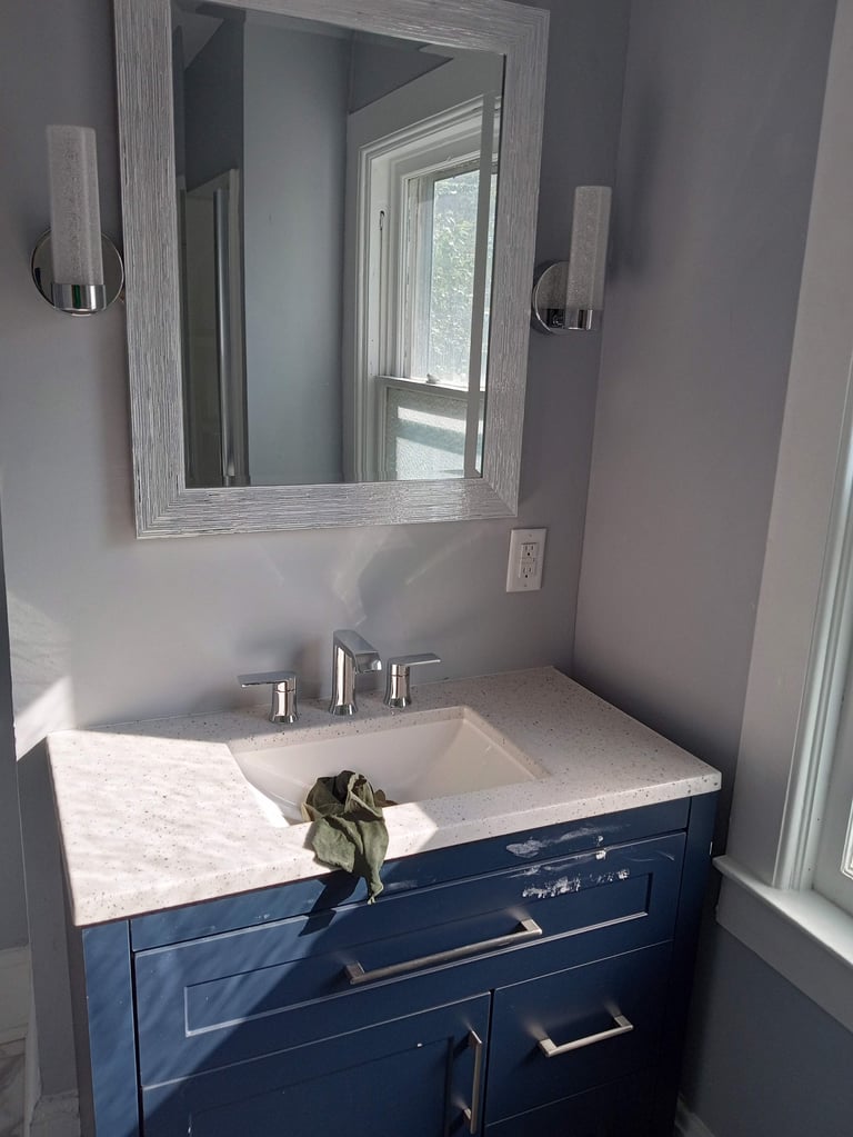 Modern bathroom vanity with white quartz countertop, dark navy cabinet, chrome faucet, framed mirror, and wall-mounted sconces