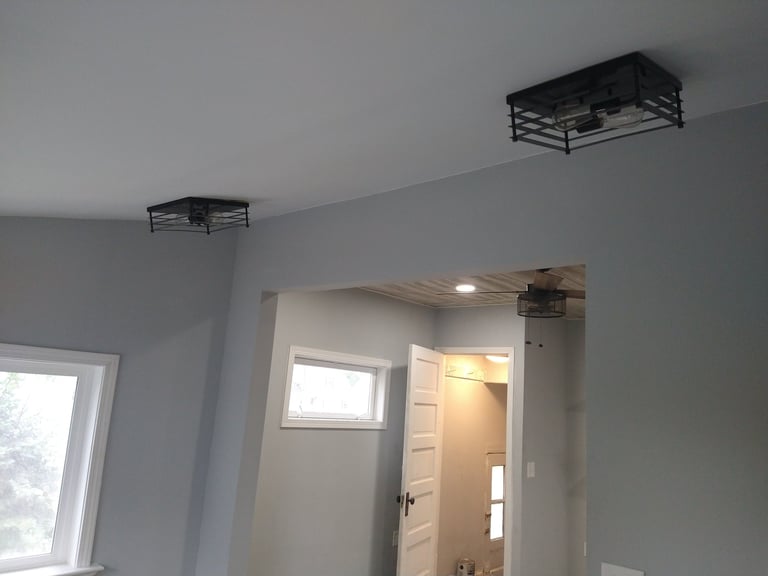 Interior room with white walls, doorway, window, and two black metal cage ceiling fixtures installed overhead