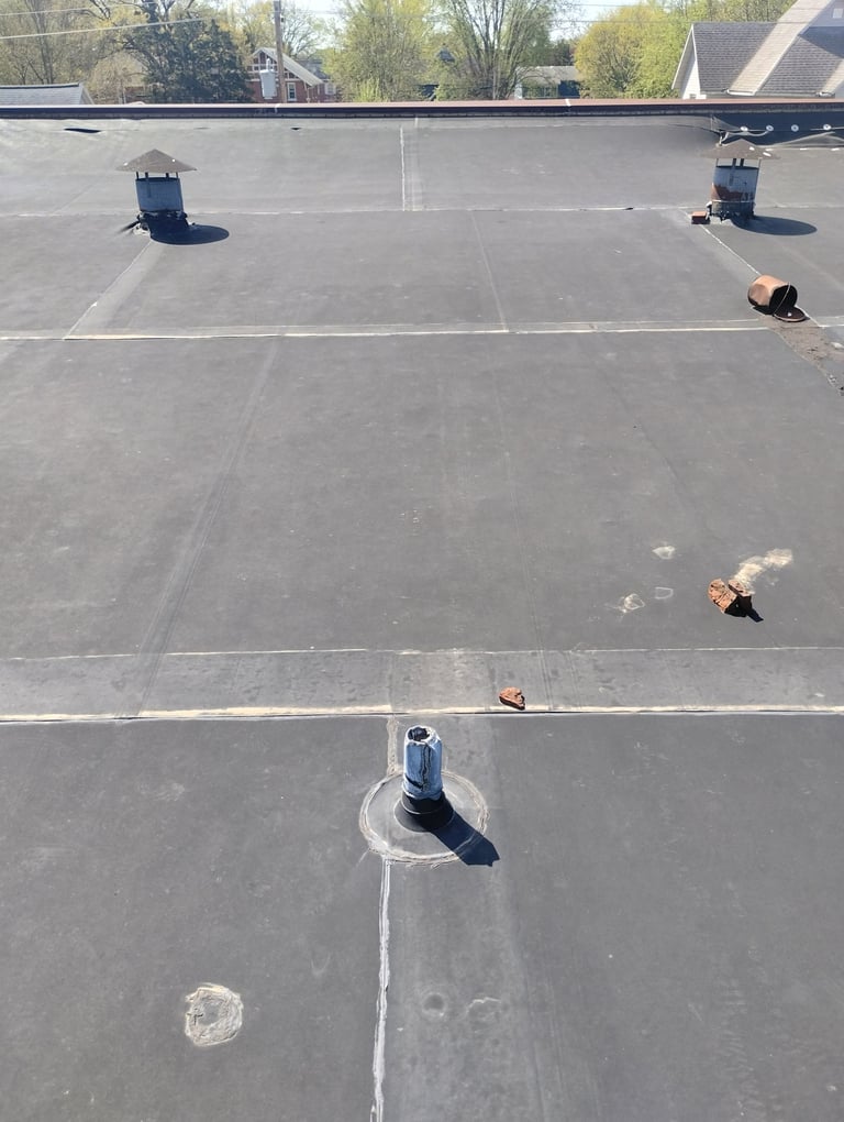 Aerial view of a flat commercial roof with ventilation pipes and equipment distributed across the asphalt surface